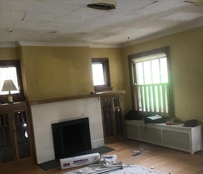 Dining room with a fireplace, yellow walls and a hole in the ceiling with debris on a tarp on the floor.