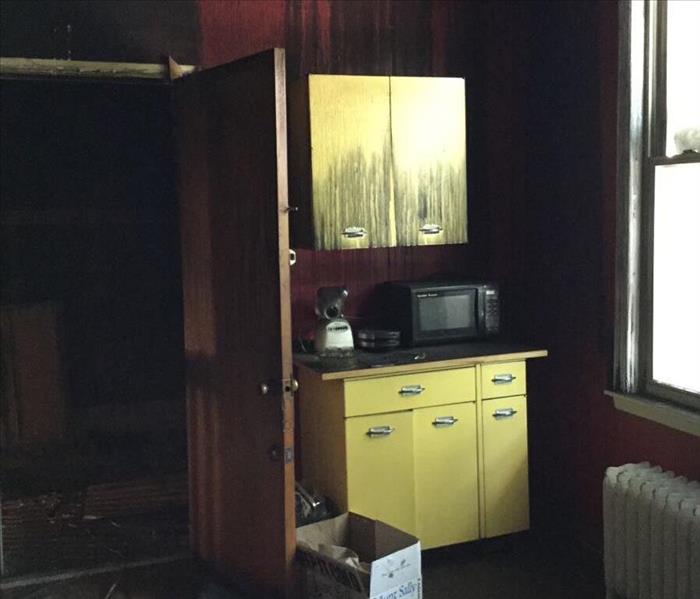 Soot covered yellow cabinets with red walls and debris on the floor of a kitchen.