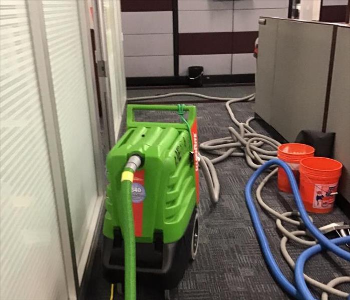 Big green water extractor in a hallway of an office with wet grey carpet and white walls with orange buckets and hoses.