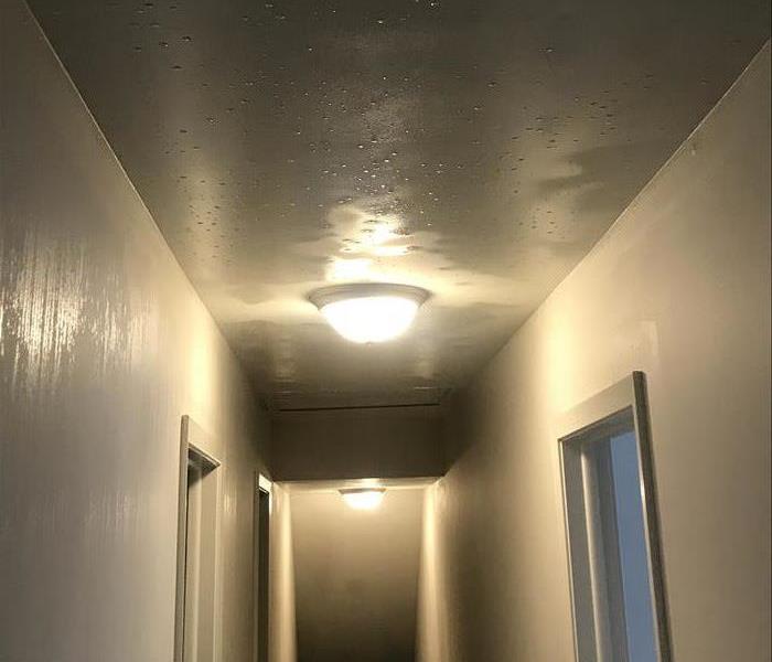 Soaking wet ceiling of a hallway with two light fixtures with white walls.