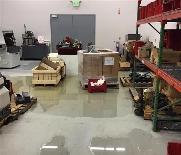 Water on the floor of a warehouse with orange shelves and boxes and wood pallets on the floor.