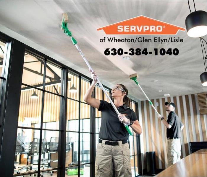 Two SERVPRO employees wiping soot off of a ceiling in an office.