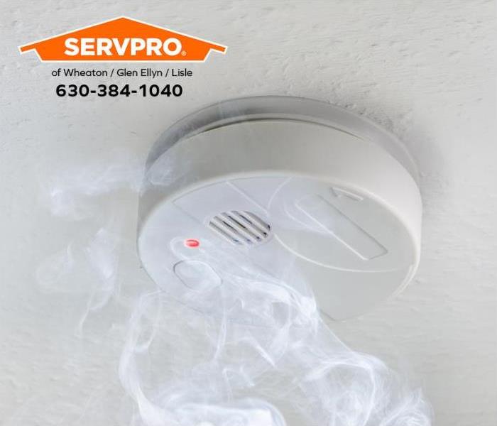 White smoke alarm with smoke on a white ceiling.