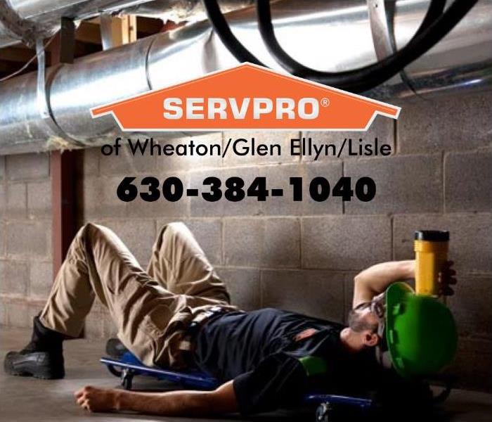 SERVPRO employee laying down with a yellow flash light looking at a silver furnace pipe.