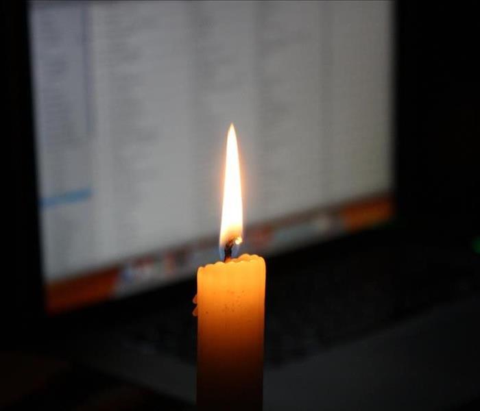 White candle burning in front of a computer screen.