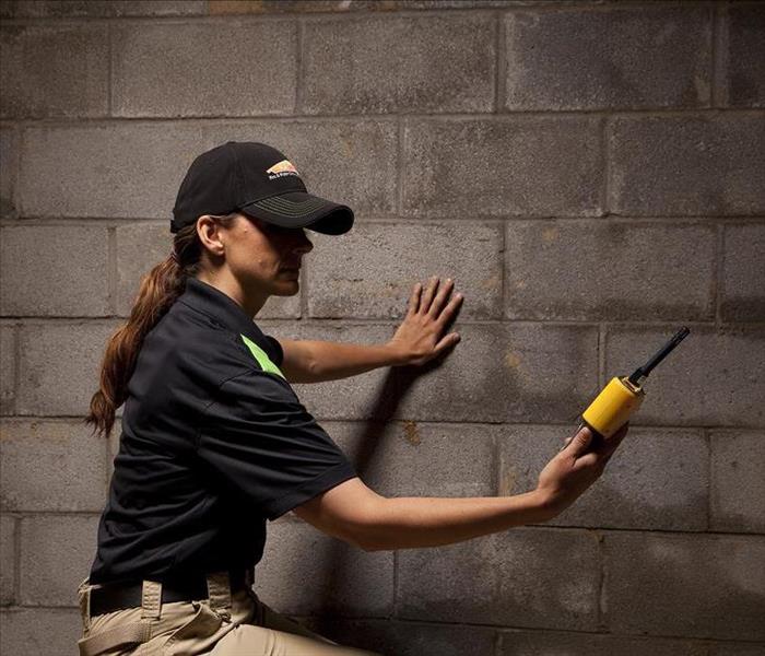 SERVPRO employee holding a yellow water meter in a basement with wet walls.