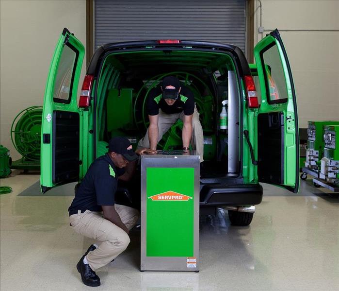 Two SERVPRO workers unloading a dehumidifier from a SERVPRO van.