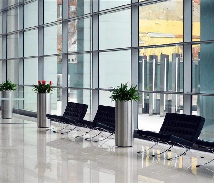 Lobby of an office building with black chairs and silver planters in front of a wall of windows.