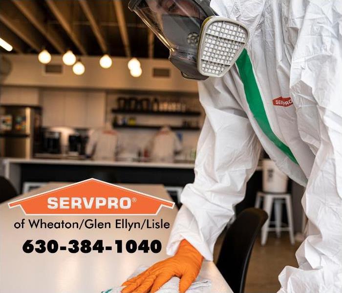 SERVPRO employee wearing PPE and wiping a table.