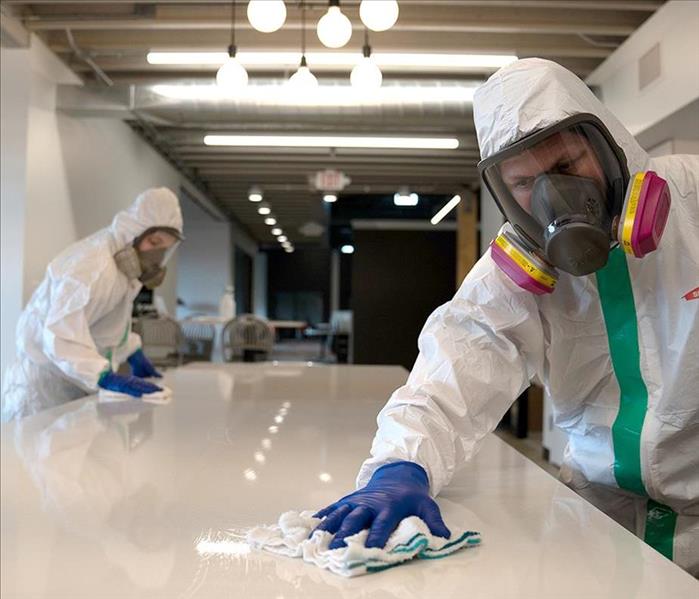 White office table being cleaned by 2 workers in white suits.