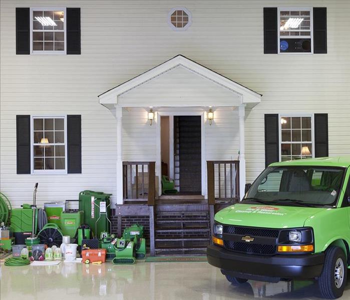 SERVPRO green van and cleaning equipment in front of a white house with black shutters.