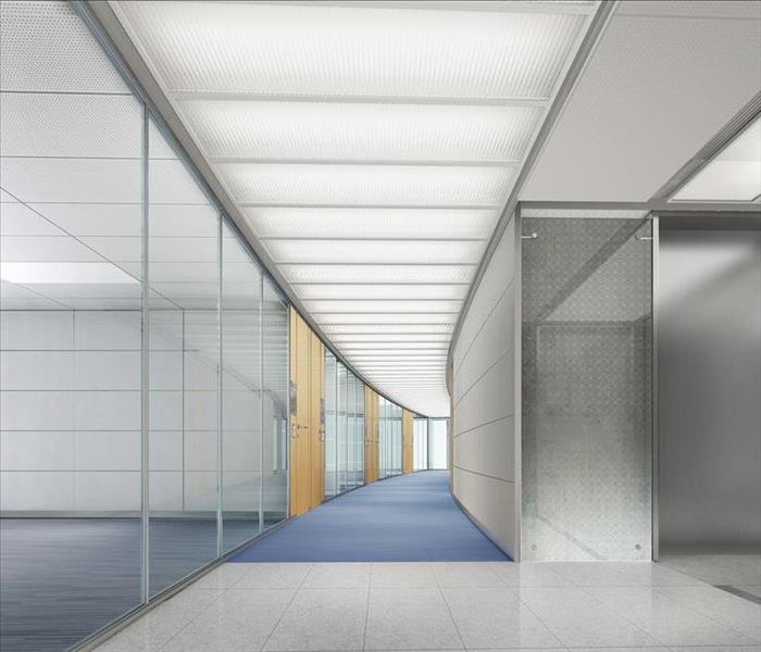 Curved hallway of an office building with blue carpet, white tile and white lights in the ceiling.