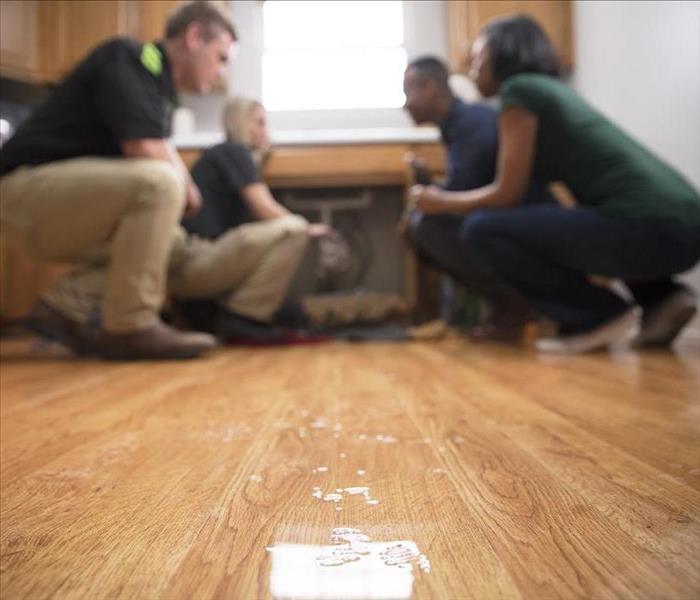 Wet wood floor with SERVPRO employees talking to customers while kneeling on the floor.