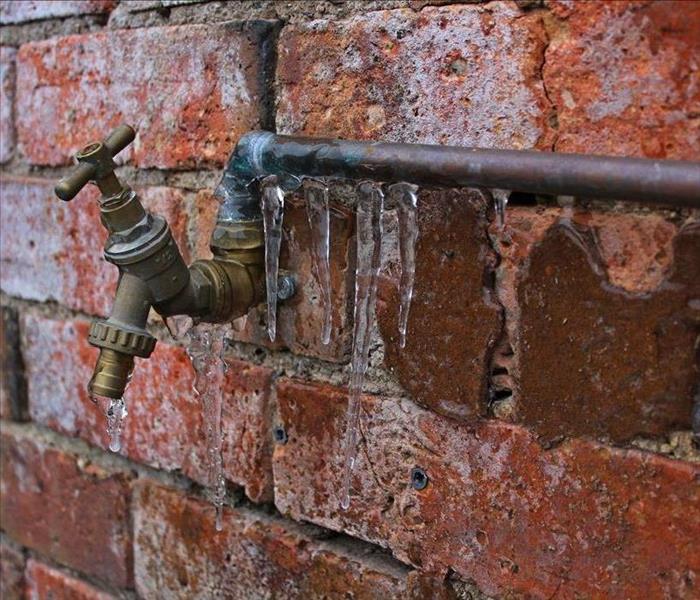 Copper water pipe on a red brick wall with frozen icicles hanging down.