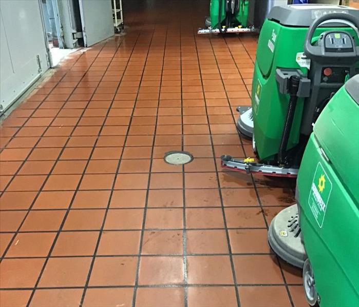 Brown tile floor of a warehouse with green cleaning machines cleaning the floor.